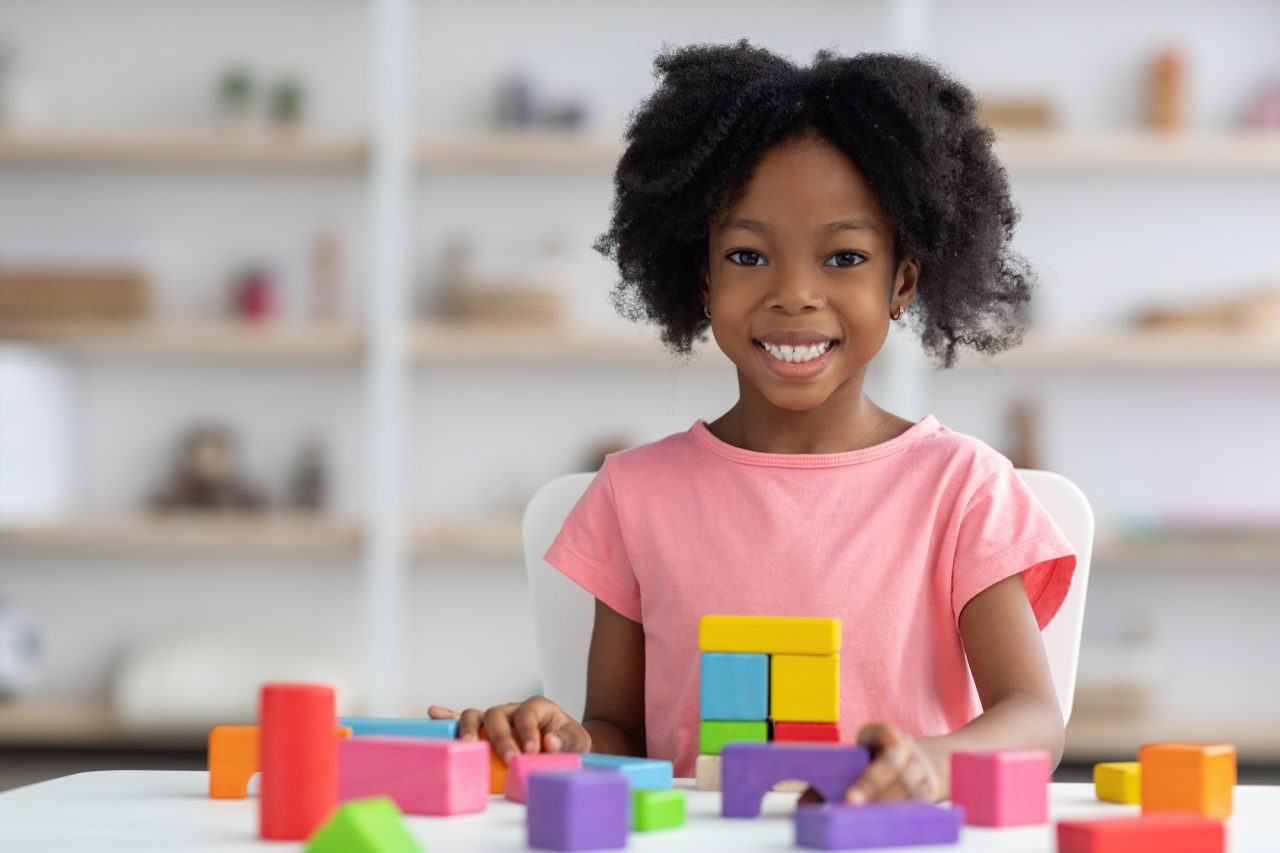 Smiling young girl playing with colorful building blocks at a table.